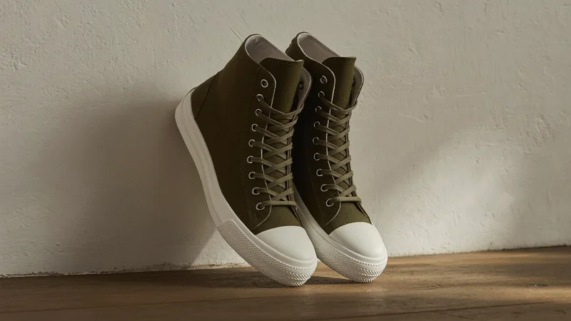 Olivengrønne lærreds-high-tops lænet mod en gipsvæg i eftermiddagslys