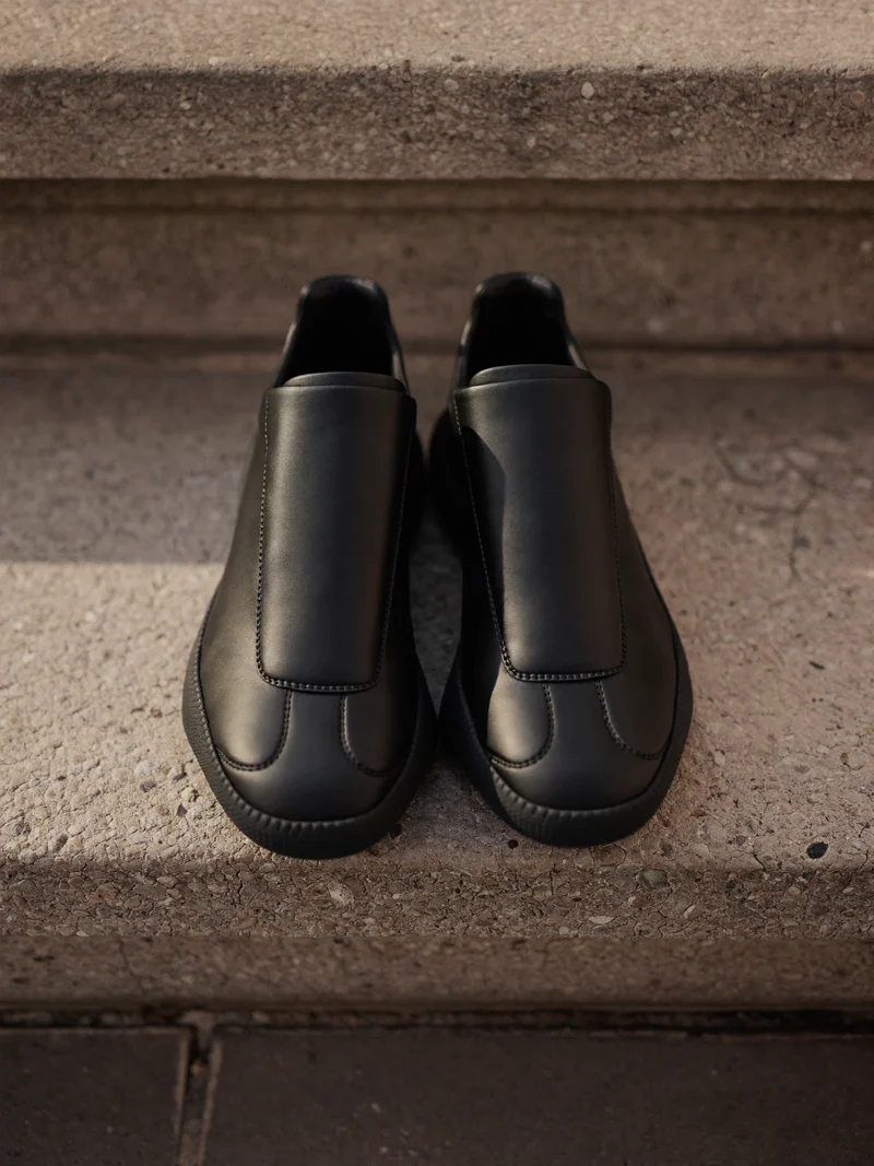 Minimalistiske sorte sneakers på et stentrin med synlig mellemsål