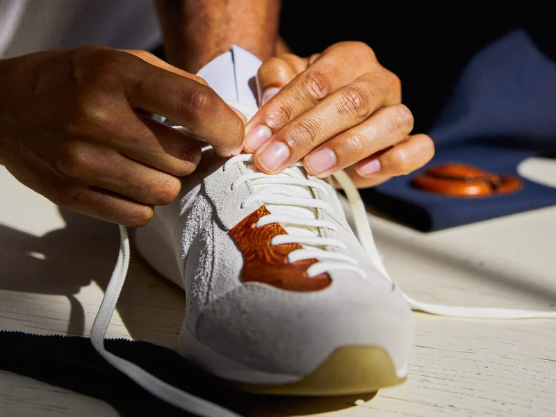 Hænder snører en sneaker ved siden af prøver af ruskind, læder og lærred