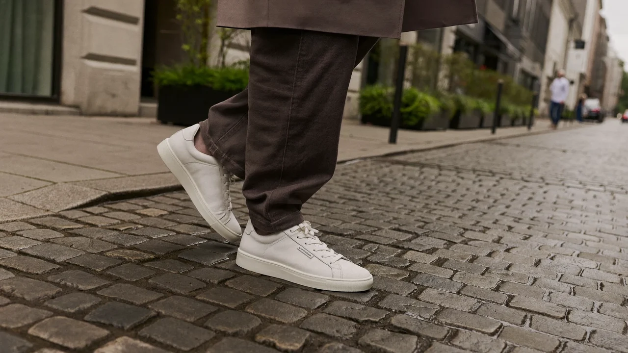 En person går i rene sneakers på brosten set i anklehøjde